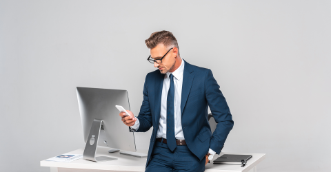 Zakenman leunt tegen bureau aan met een telefoon in zijn hand